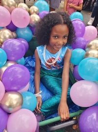 a little girl sitting in a cart filled with balloons